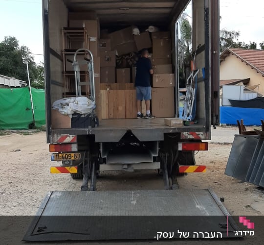 משאית פתוחה עם קרטונים ואדם מסדר בפנים